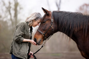 woman forehead to forehead standing in front of dark brown horse