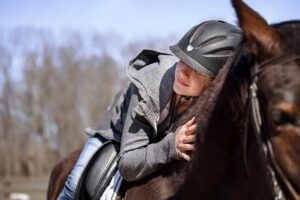 young woman lying on horse wearing safety helmet and gear hugging him